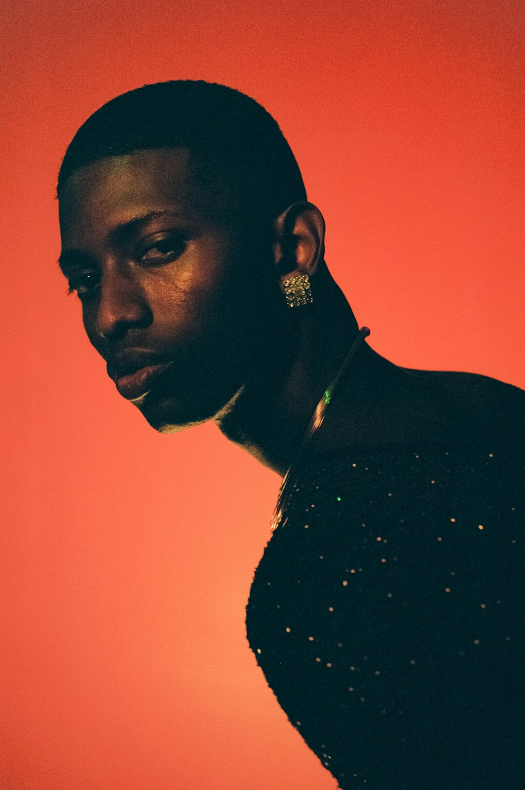 Studio portrait of a young man with headphones around his neck on an orange background