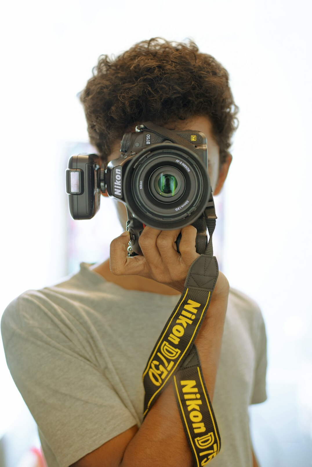 Studio portrait of a young man with a camera strap on a yellow background